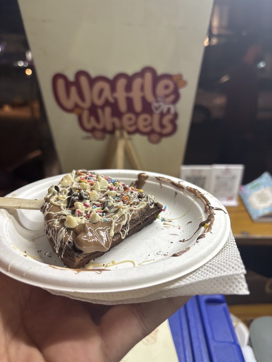 A chocolate-dipped waffle on a stick with white drizzle and sprinkles